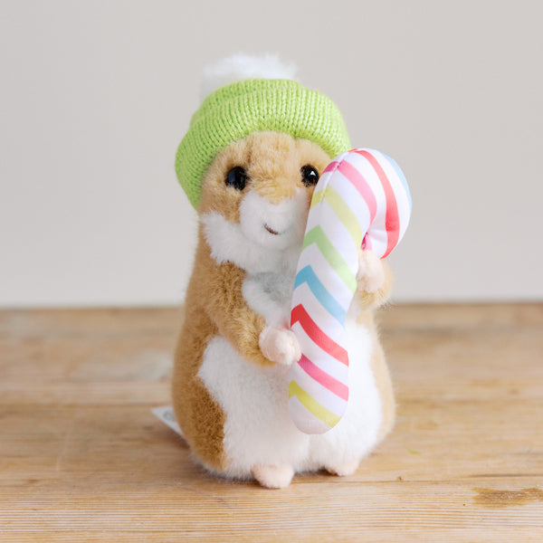 A plush toy hamster stuffed animal with a green knitted hat holding a striped candy cane.